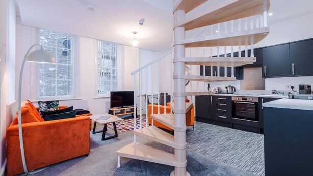 A modern interior with a spiral staircase, a kitchen, and a living area with orange furniture.