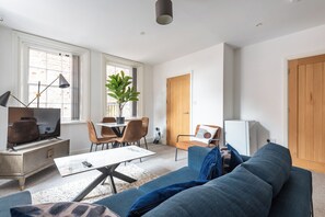 A modern living room with a sofa, TV, dining table, chairs, and a plant.