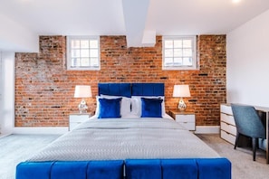 A bedroom with a brick wall, a bed with blue bedding, two bedside tables with lamps, and a desk with a chair. - Old Dutch Embassy by Guestz (Hull)