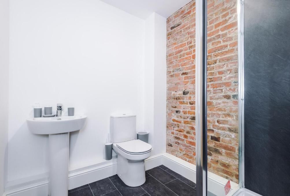 Een badkamer met een wit wastafelmeubel, toilet en een bakstenen muur.