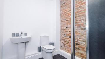 Een badkamer met een wit wastafelmeubel, toilet en een bakstenen muur.