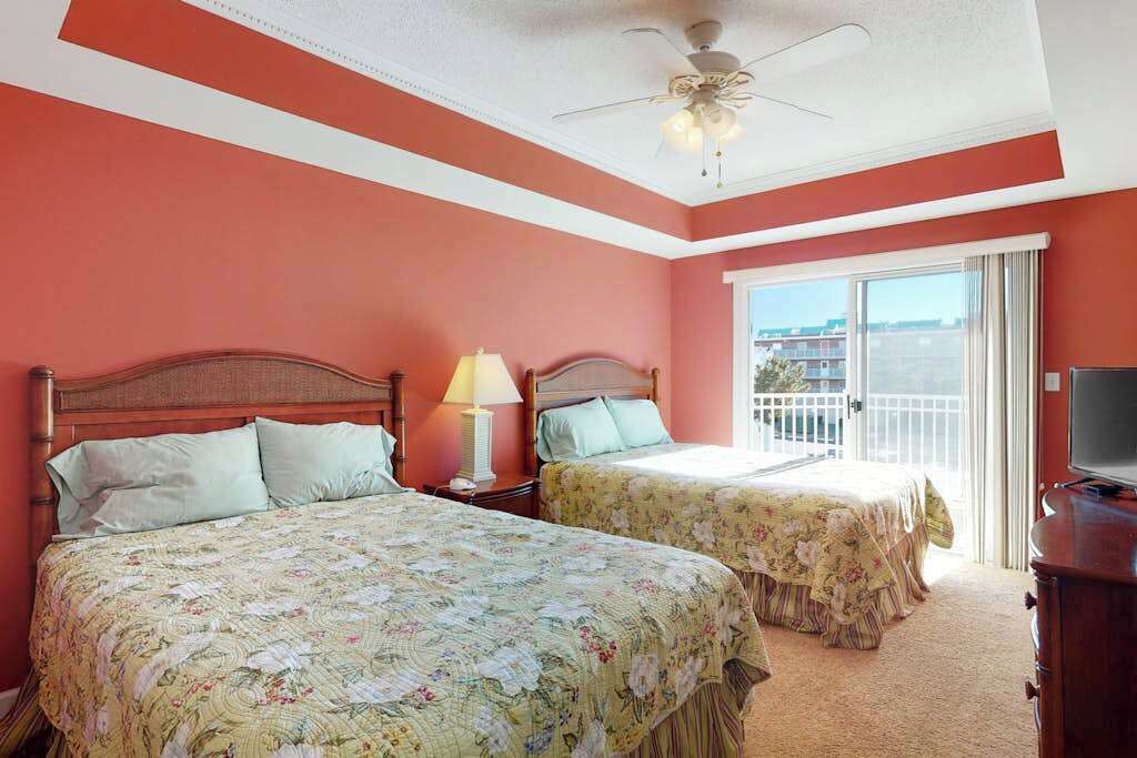 A hotel room with two beds, a ceiling fan, a TV, and a balcony with a view.