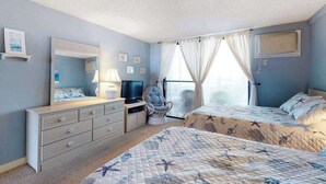 Um quarto com uma cama, cômoda, cadeira, escrivaninha com uma TV e janela com cortinas.