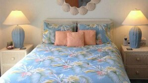 A bed with floral bedding, two bedside lamps, a mirror, and a nightstand with a phone and a vase. - Condo 3 Blocks from the Beach w/ Sunny Patio, Central AC, WiFi & Shared Pool (Ocean City)