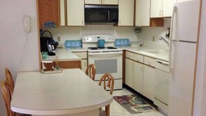 A compact kitchen with white cabinets, a microwave, a stove, a sink, and a dining table with chairs. - Condo 3 Blocks from the Beach w/ Sunny Patio, Central AC, WiFi & Shared Pool (Ocean City)