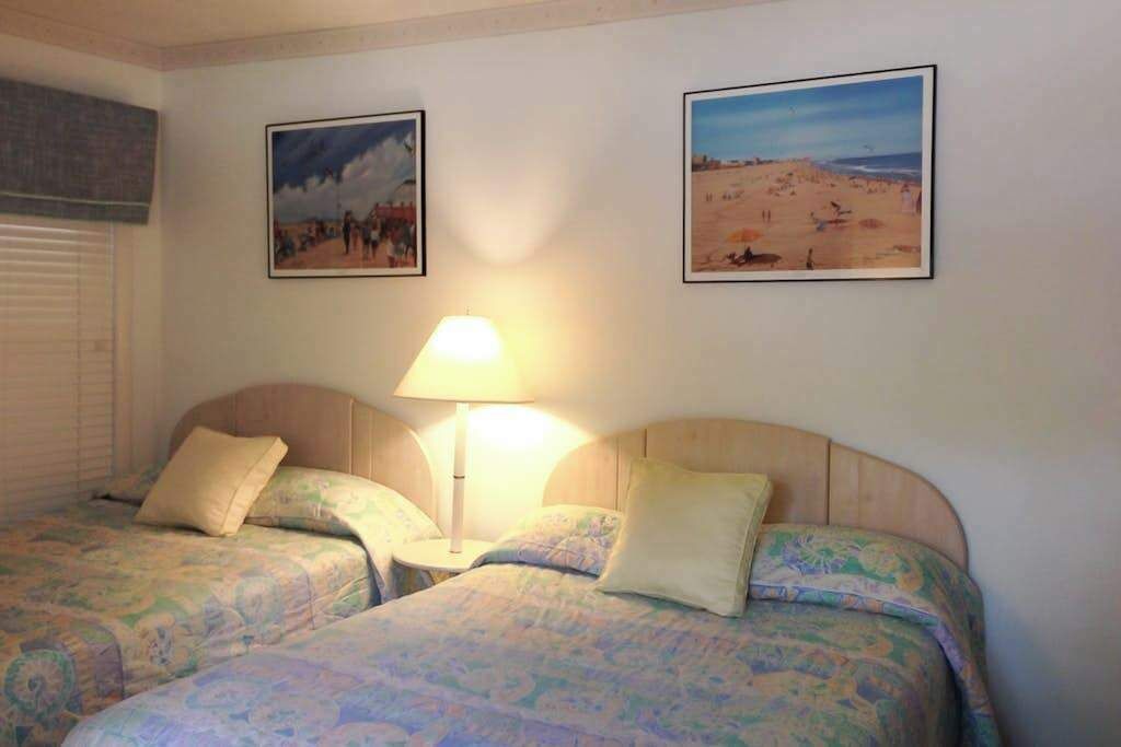 A room with two beds, a lamp, and two framed pictures on the wall.