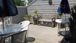 An outdoor patio area with a round table, two chairs, a bench, and umbrellas. - Condo 3 Blocks from the Beach w/ Sunny Patio, Central AC, WiFi & Shared Pool (Ocean City)
