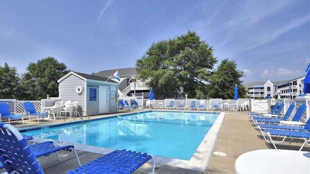 A swimming pool with blue lounge chairs and a small building with a lifebuoy. - Condo 3 Blocks from the Beach w/ Sunny Patio, Central AC, WiFi & Shared Pool (Ocean City)