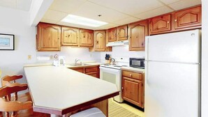 Una cocina con armarios de madera, un refrigerador blanco, un microondas y una mesa de comedor con sillas.
