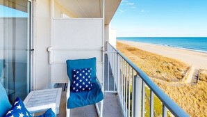Un balcón con vista a la playa, una silla con un cojín estampado de estrellas y una mesa con un cojín estampado de estrellas.