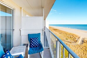 A balcony with a view of the beach, a chair with a star-patterned pillow, and a table with a star-patterned pillow. - Well-Equipped Family Beachfront Condo w/Balcony, Views, Washer/Dryer, A/C, WiFi (Ocean City)