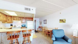 Una cocina compacta con armarios de madera, una isla central con taburetes, un sillón azul y una mesa de comedor.