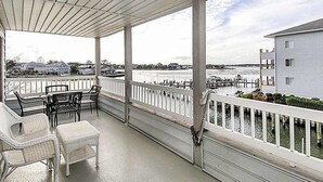 A covered porch with white railings, wicker furniture, and a view of a dock and water. - Waterfront condo with pool, balcony, fireplace, central AC, & washer/dryer (Ocean City)