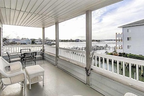 A covered porch with white railings, wicker furniture, and a view of a dock and water. - Waterfront condo with pool, balcony, fireplace, central AC, & washer/dryer (Ocean City)