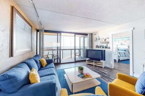 Un salon moderne avec un canapé, une table basse et un téléviseur, un balcon avec vue et une chambre à coucher avec un lit et une fenêtre.