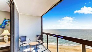 A balcony with a view of the beach, two chairs, a lamp, and a decorative item. - Cozy beachfront condo with balcony views, pools & game room (Ocean City)