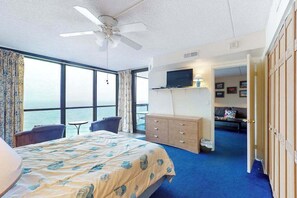 A hotel room with a bed, a desk, a chair, a television, a wardrobe, and a view of the sea. - Stunning beach condo with balcony, angled views, W/D, pools & gym (Ocean City)