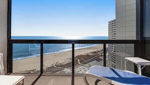Ein Balkon mit Blick auf Strand und Meer, ein Sessel und ein kleiner Tisch.