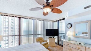 Hotellihuone, jossa on sänky, tuoli, televisio, lipasto ja kattotuuletin.