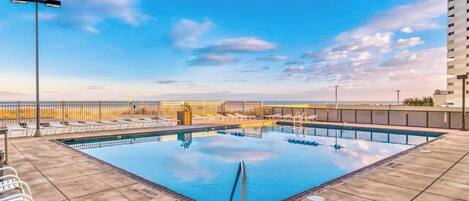 A rooftop pool with a clear view of the city skyline, a covered seating area, and a tall building in the background.