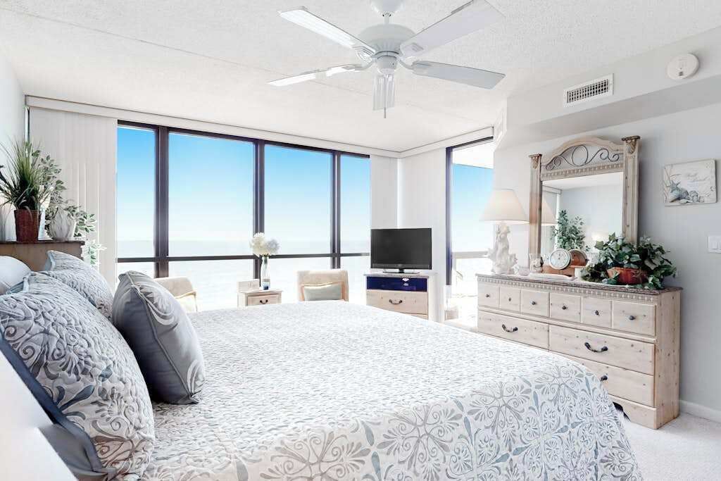 Ein Schlafzimmer mit einem großen Bett, einem Fernseher, einer Kommode und Blick aufs Meer.