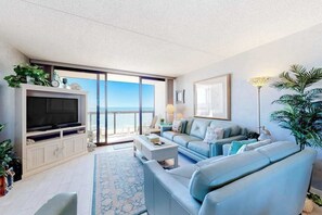 A living room with a television, sofa, coffee table, and a view of the ocean. - Classic beachfront condo with pools, beach bar, tennis & AC (Ocean City)