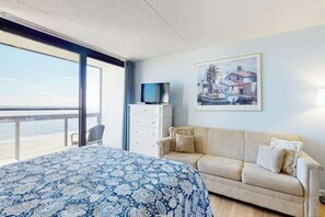 Ein Hotelzimmer mit einem großen Bett, einem beigefarbenen Sofa, einem Fernseher auf einer Kommode und einem Bild an der Wand.