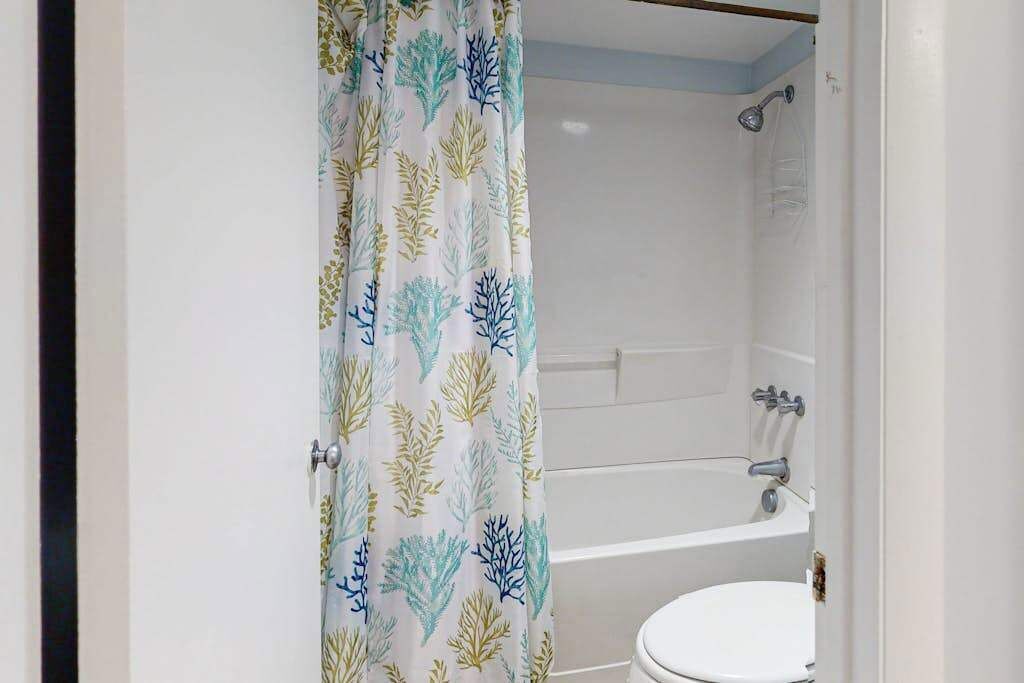 A bathroom with a shower, toilet, and a curtain with a leaf pattern.