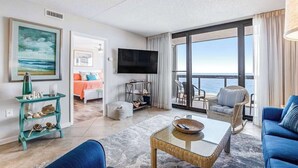 Ein Wohnzimmer mit großem Fernseher, einem Esstisch, einer Couch und Blick auf den Ozean.