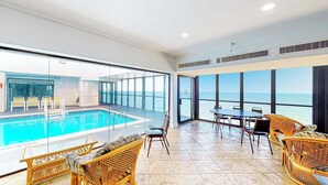 Ein geräumiger Innenbereich mit Pool, Korbmöbeln und großen Fenstern mit Meerblick.
