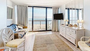 Ein Hotelzimmer mit Balkon, einer Couch, einem Fernseher, einem Schminktisch und einem Stuhl.