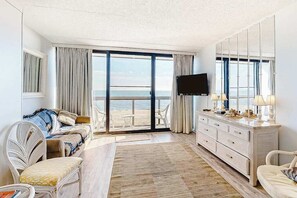 Ein Hotelzimmer mit Balkon, einer Couch, einem Fernseher, einem Schminktisch und einem Stuhl.