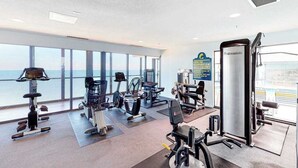 Ein Fitnessstudio mit unterschiedlichen Trainingsgeräten, großen Fenstern und Meerblick.