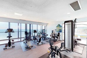 Ein Fitnessstudio mit unterschiedlichen Trainingsgeräten, großen Fenstern und Meerblick.