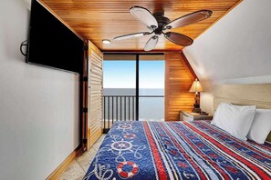 Ein Schlafzimmer mit Bett, Deckenventilator, Nachttisch, Lampe und Blick auf den Himmel.