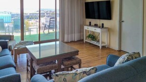 Un salon avec une table à plateau en verre, des fauteuils en osier, un canapé, un téléviseur et une vue sur la ville.