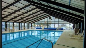 Une piscine intérieure avec des parois en verre transparent, de l’eau bleue et des chaises longues.