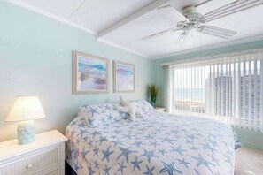 Ein Schlafzimmer mit einem Bett, einem Nachttisch, einer Lampe, einem Deckenventilator und zwei gerahmten Bildern an der Wand.
