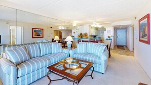 A living room with striped sofas, a glass coffee table, and a kitchen in the background. - English Towers 205 (Ocean City)