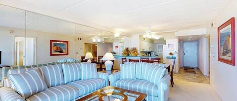 Ein Wohnzimmer mit gestreiften Sofas, einem Glastisch und einer Küche im Hintergrund.
