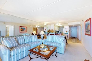 Ein Wohnzimmer mit gestreiften Sofas, einem Glastisch und einer Küche im Hintergrund.