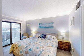 A bedroom with a bed, two bedside tables with lamps, a painting, and a balcony with a view. - Family-Friendly Condo w/Private Balcony, Washer/Dryer, Cable, and Central A/C (Ocean City)