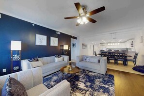 Ein modernes Wohnzimmer mit zwei Sofas, einem Couchtisch, einem Deckenventilator und einem Essbereich im Hintergrund.