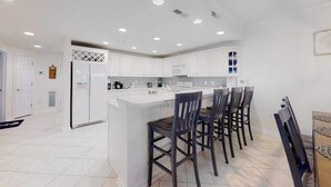 Una cocina moderna con armarios blancos, una isla central con taburetes y luces empotradas en el techo.
