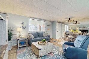 A living room with a sofa, coffee table, and a dining area with chairs and a table. - Colonial Condo 102 (Ocean City)