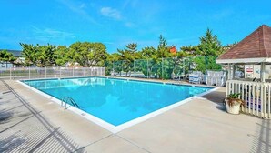 A rectangular swimming pool with a clear blue water surface, surrounded by a white fence, and a small building with a brown roof to the right. - Club Ocean Villa II 97 (Ocean City)