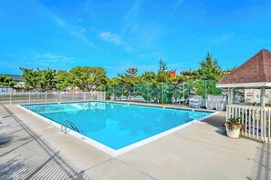 A rectangular swimming pool with a clear blue water surface, surrounded by a white fence, and a small building with a brown roof to the right. - Club Ocean Villa II 97 (Ocean City)