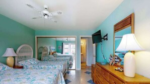 A hotel room with a ceiling fan, a TV mounted on the wall, a wooden dresser, and a bed with floral bedding. - Club Ocean Villa II 97 (Ocean City)