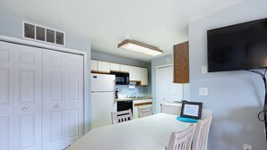 A compact kitchen with white cabinets, a microwave, and a built-in oven. There's a dining table with chairs, a flat-screen TV mounted on the wall, and a ceiling vent. - Club Ocean Villa II 97 (Ocean City)