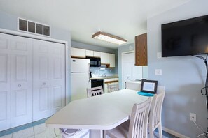 A compact kitchen with white cabinets, a microwave, and a built-in oven. There's a dining table with chairs, a flat-screen TV mounted on the wall, and a ceiling vent. - Club Ocean Villa II 97 (Ocean City)
